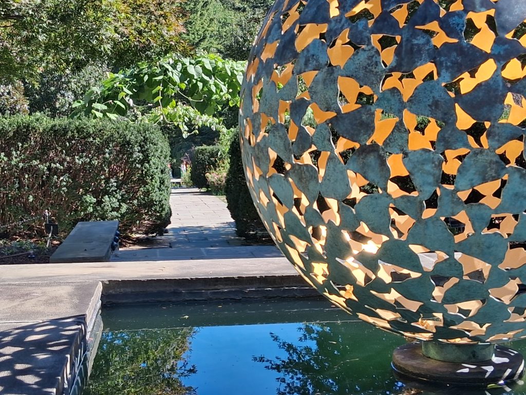 Spherical metal sculpture with butterfly-shaped openings above a reflecting pool at Brookside Gardens.