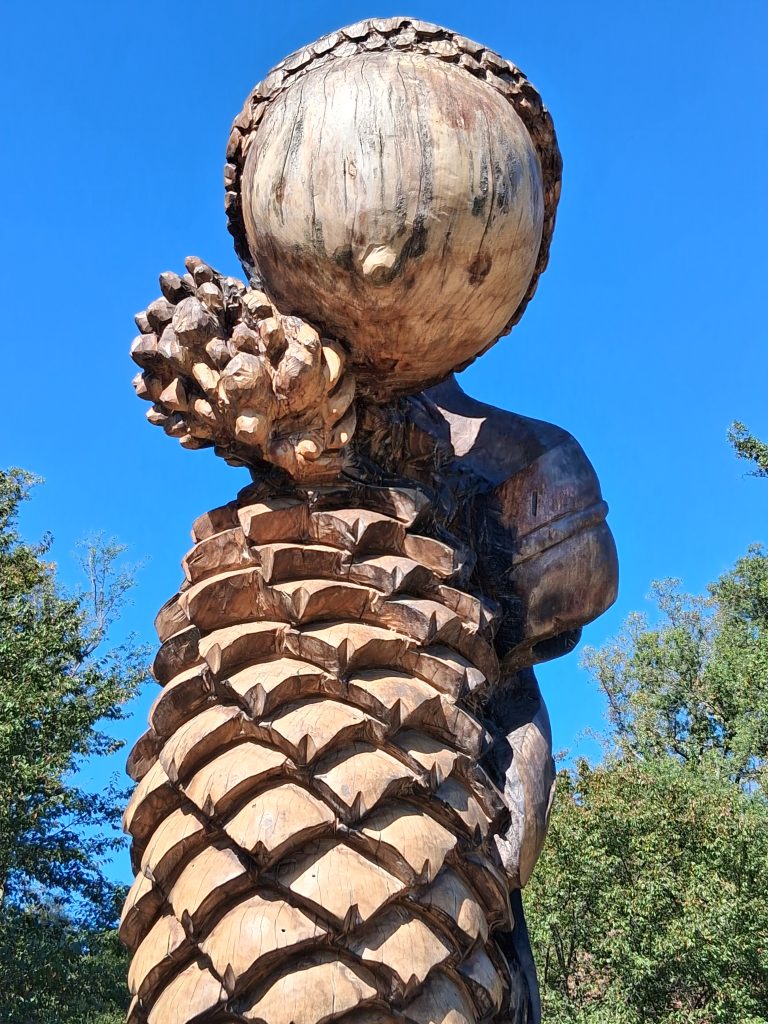 Tall wooden sculpture carved with an acorn and pine cones against a clear blue sky at Brookside Gardens.
